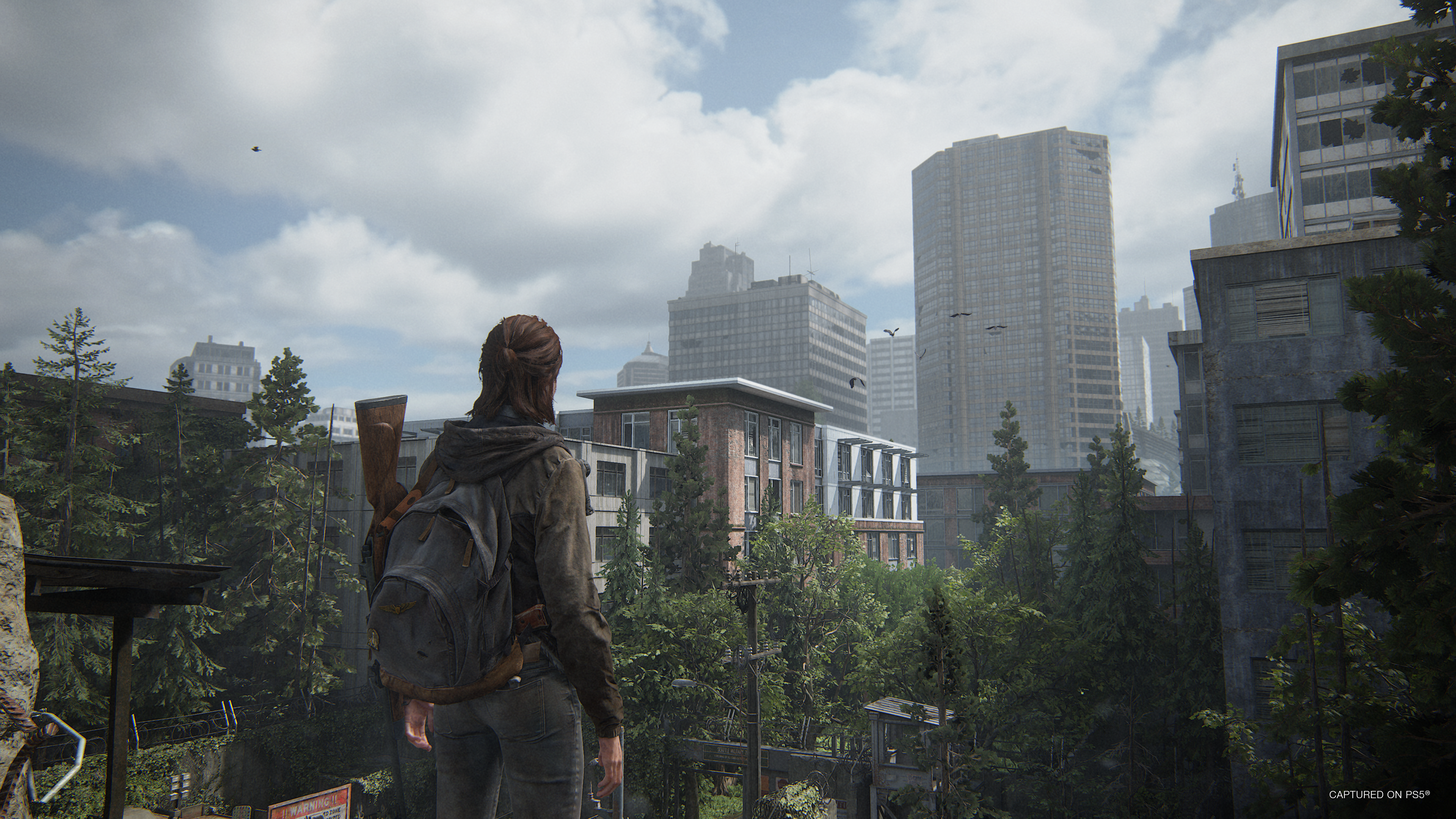 Eine Frau mit Rucksack steht auf einem Dach mit Blick auf eine Stadt mit Wolkenkratzern.