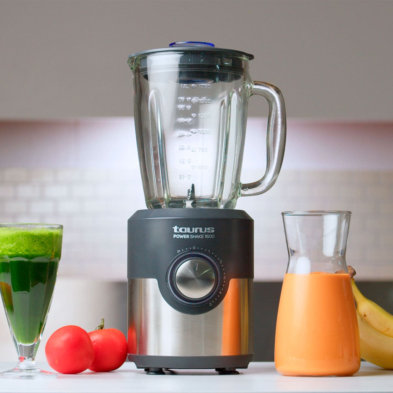 Licuadora con jarra de vidrio y vaso al lado con jugo de naranja y vaso con jugo verde.