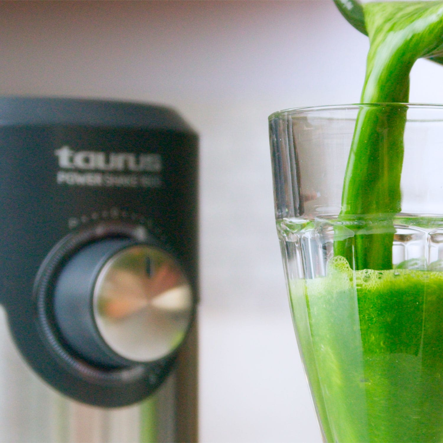 Jugo verde vertiéndose en un vaso, con una licuadora en el fondo.