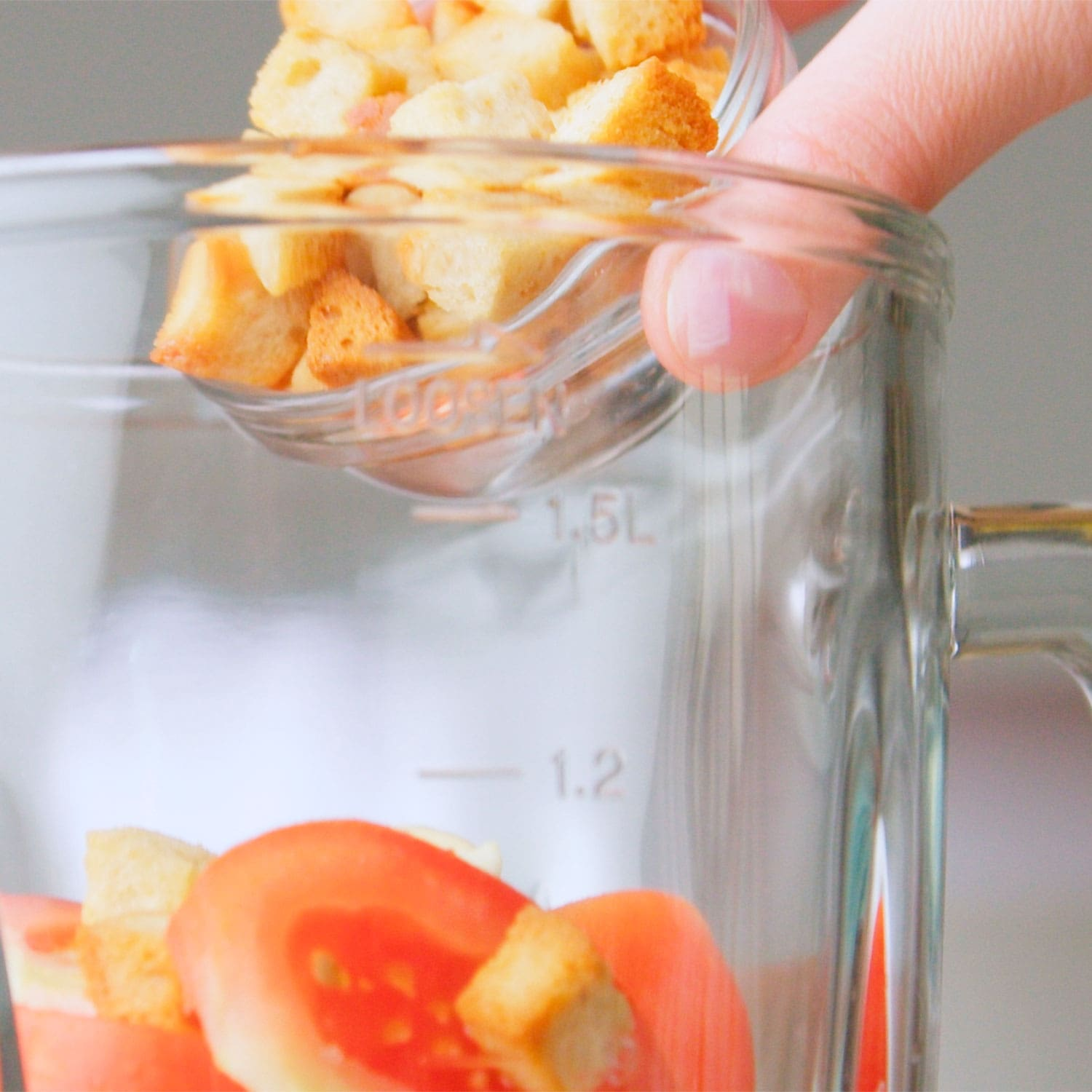 Crutones vertiéndose en una licuadora transparente con tomates y otros ingredientes.