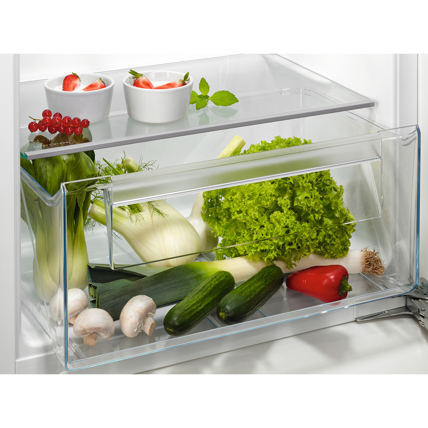 Un cassetto del frigorifero pieno di verdure: lattuga, cetrioli, funghi, peperoni e fragole.