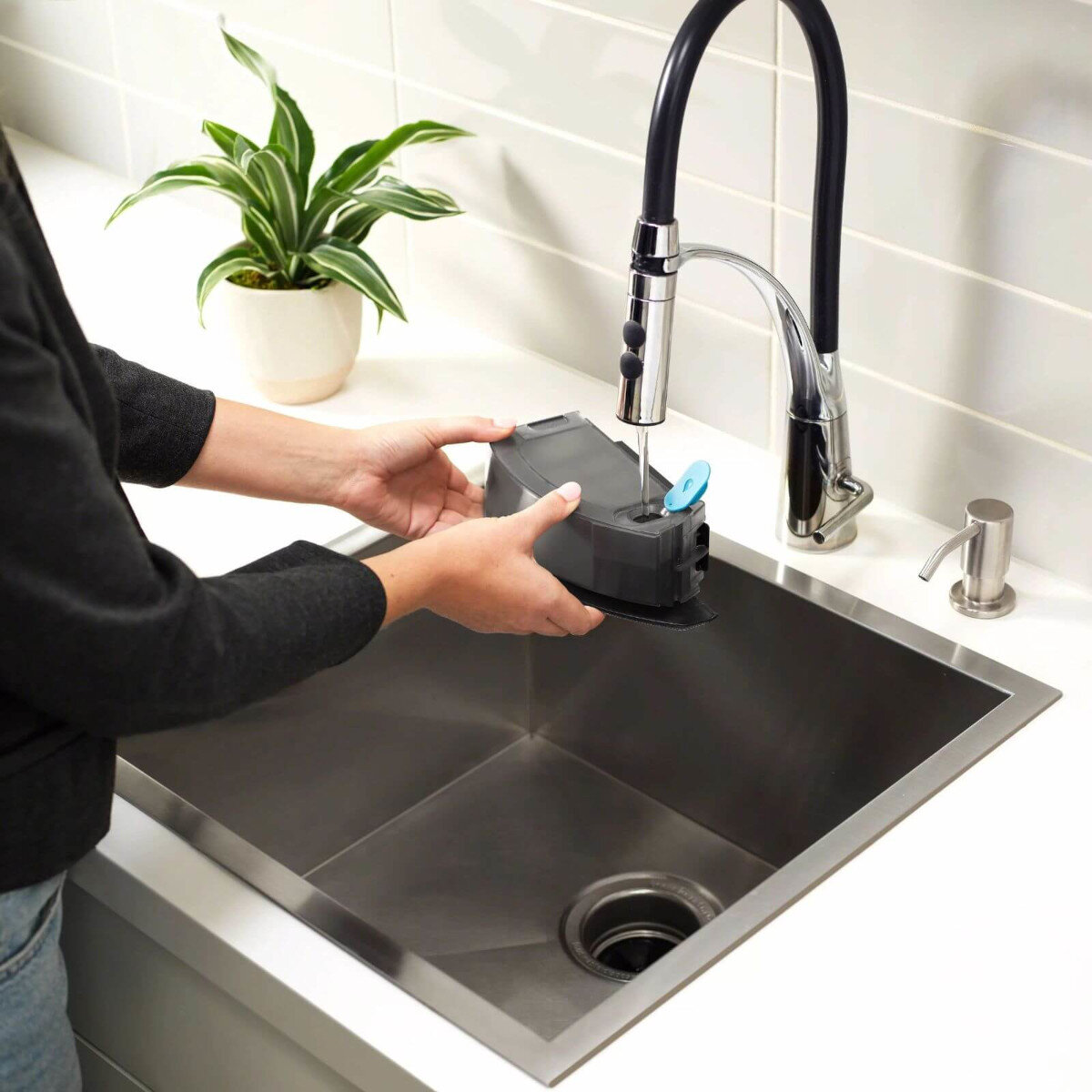 Ręce osoby umieszczającej czarne urządzenie w zlewozmywaku kuchennym. W pobliżu kran.