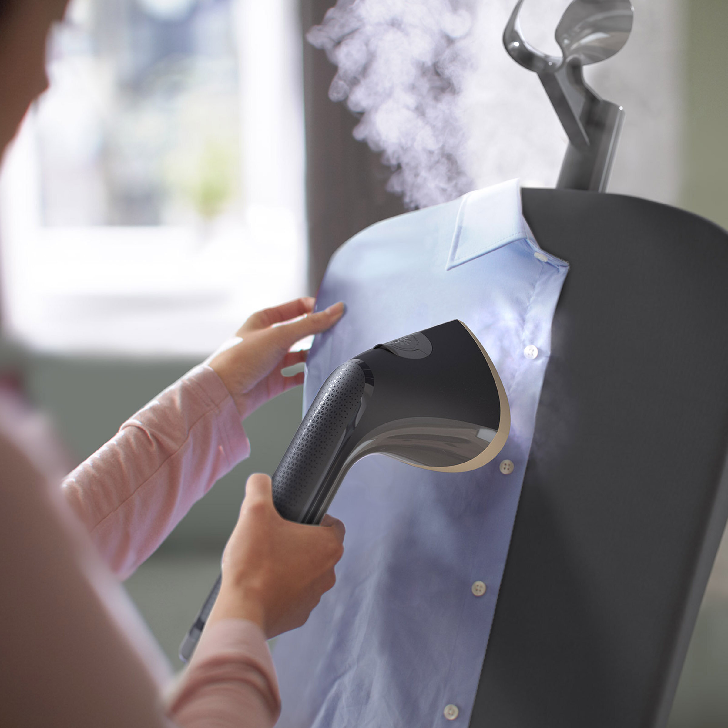 Osoba parująca jasnoniebieską koszulę na szarym parowarze do ubrań, widok z bliska.