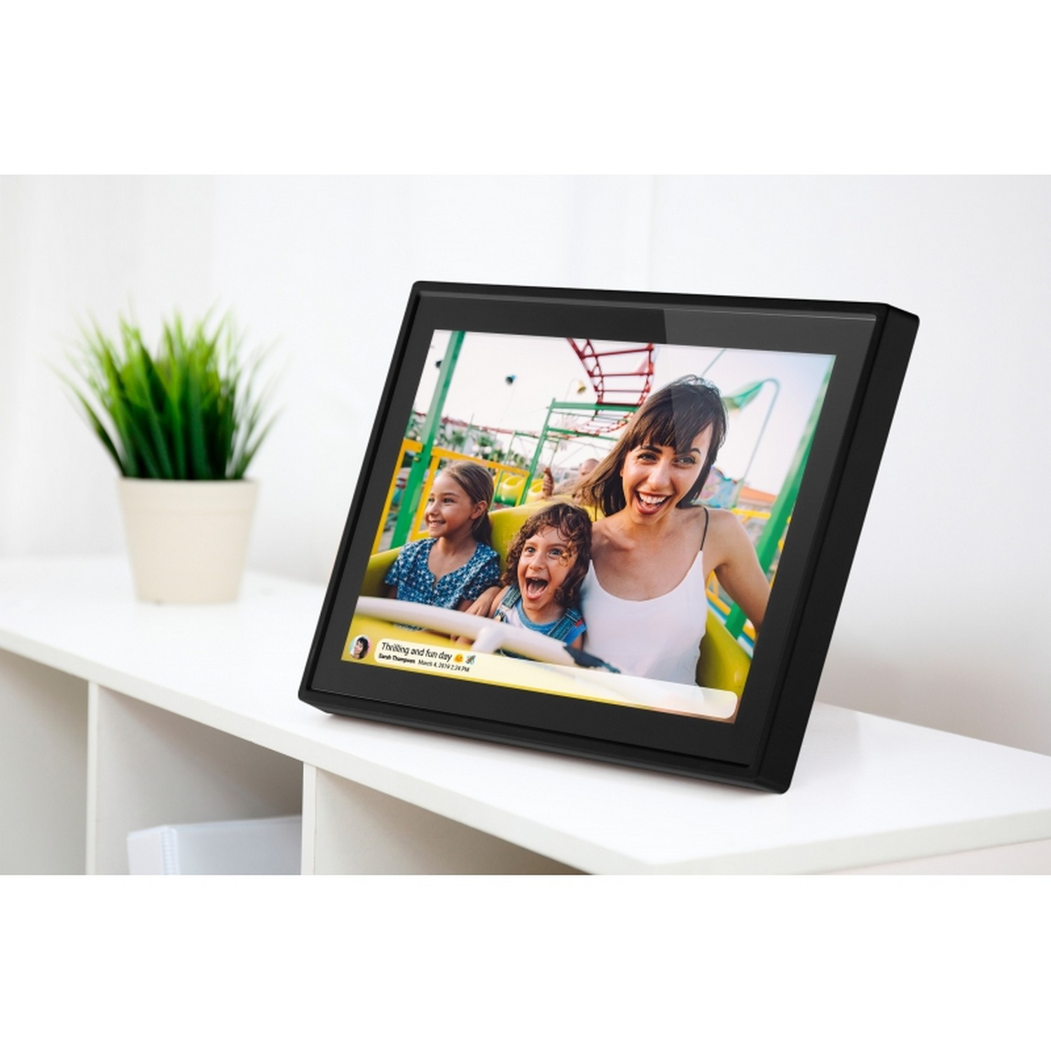 Digital photo frame displaying a photo of a family on a roller coaster, on a white shelf.