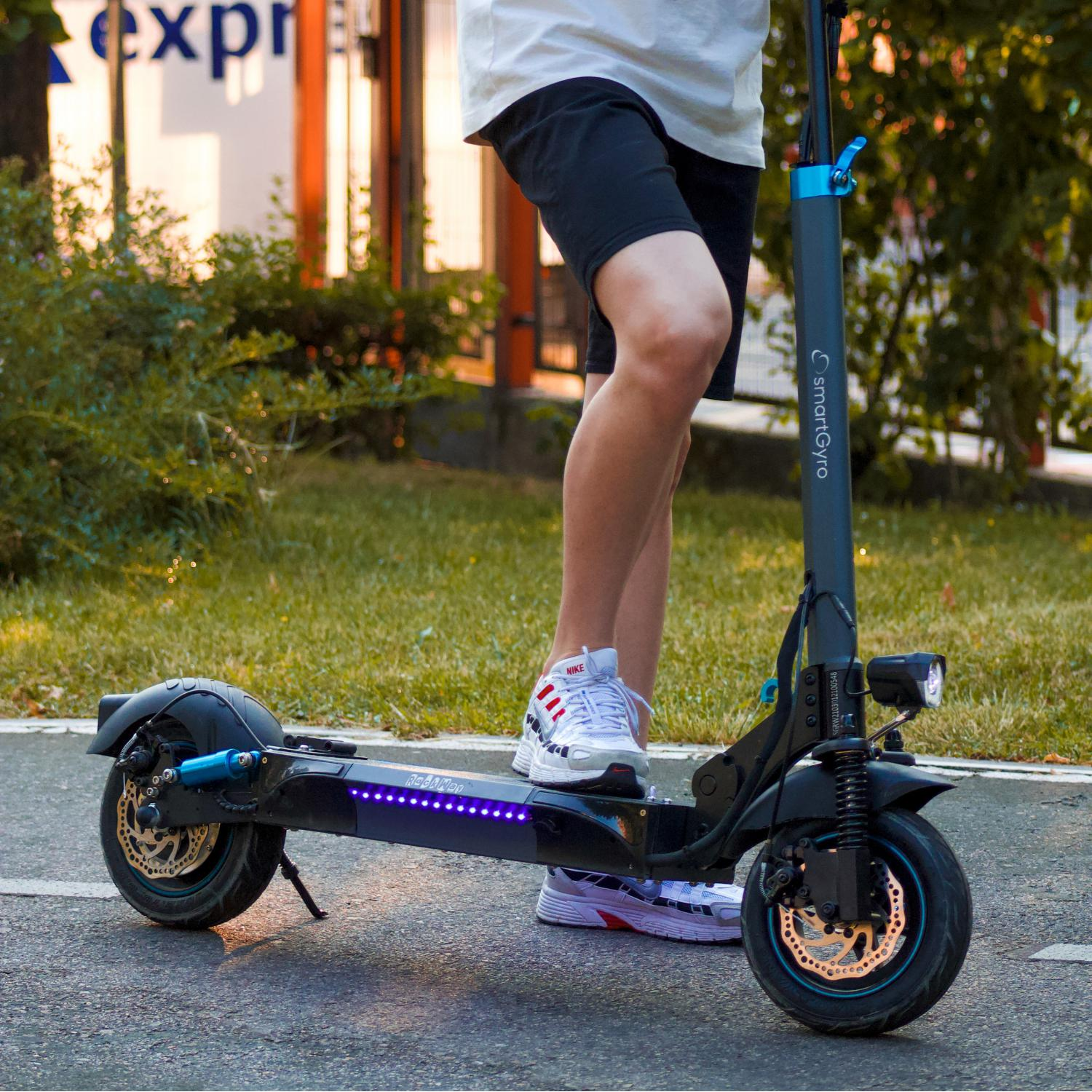 Una persona en un scooter eléctrico en una carretera pavimentada. El scooter es negro y azul, con la marca 'SmartGyro'.