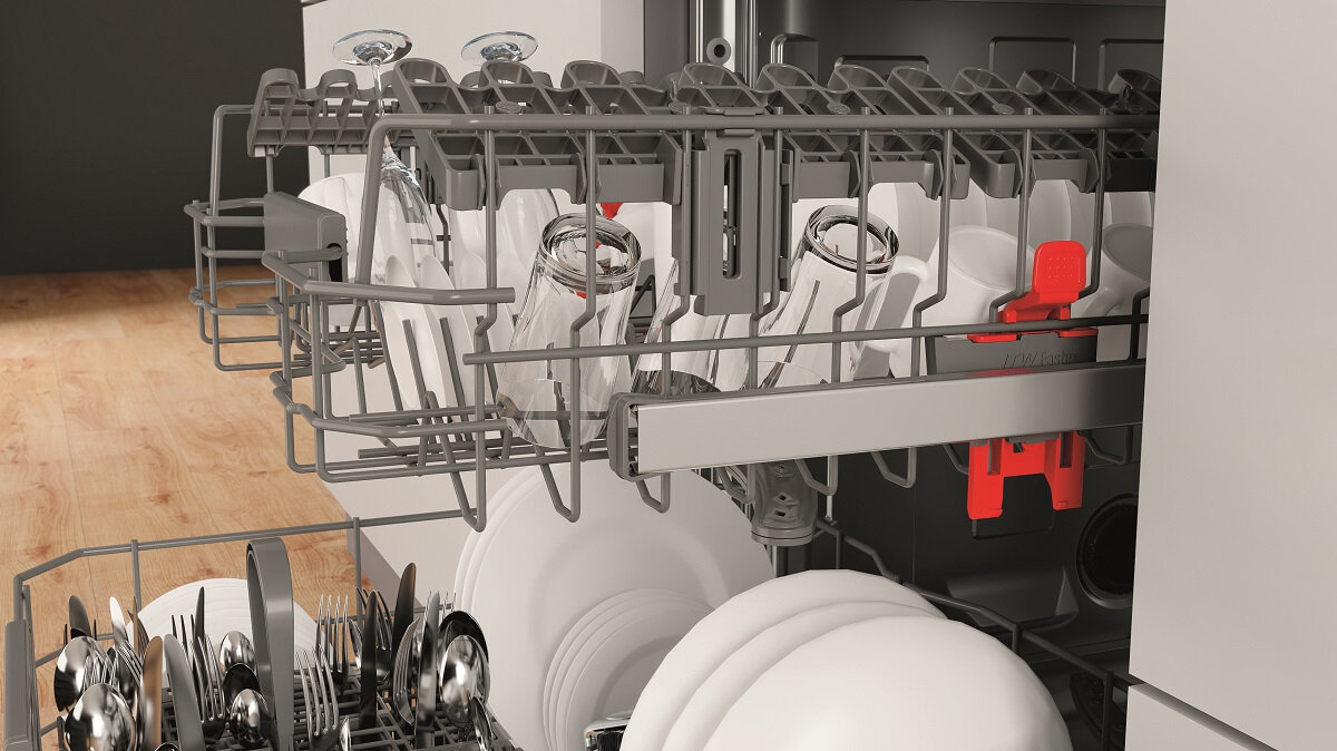 Wnętrze zmywarki ze szklankami, talerzami i sztućcami, z czerwonymi akcentami.