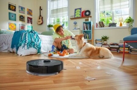 Chłopiec bawiący się z psem i odkurzaczem robota na drewnianej podłodze w pokoju.