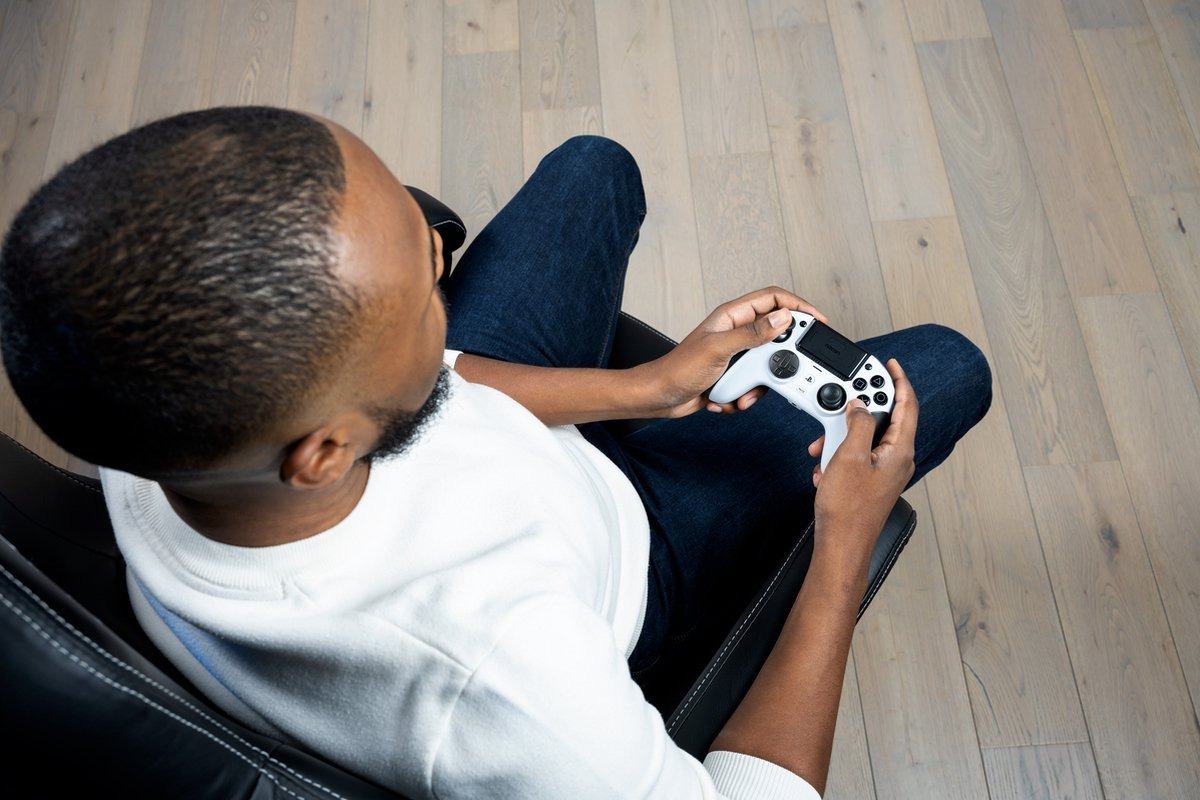 Homme assis dans une chaise, tenant une manette de jeu blanche, jouant à un jeu.