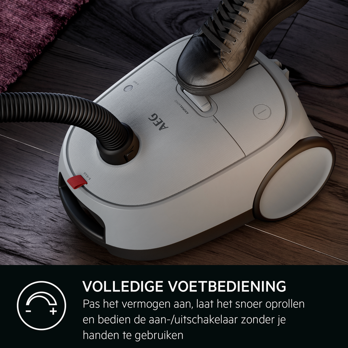 Een wit en grijze stofzuiger met een voetbediende aan/uit-knop, op een houten vloer.