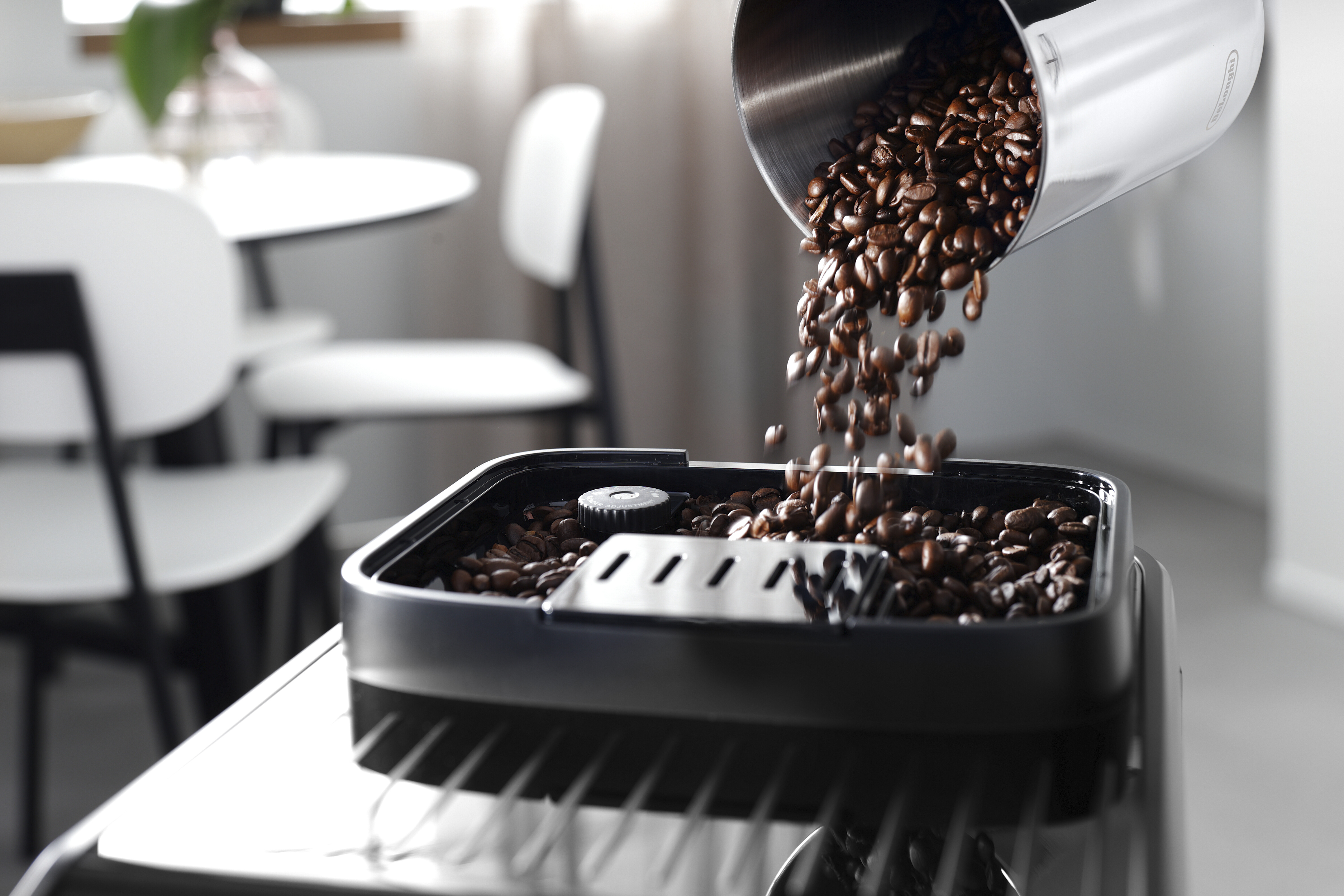 Granos de café vertiéndose desde un recipiente metálico a una bandeja negra de cafetera. Interiores.