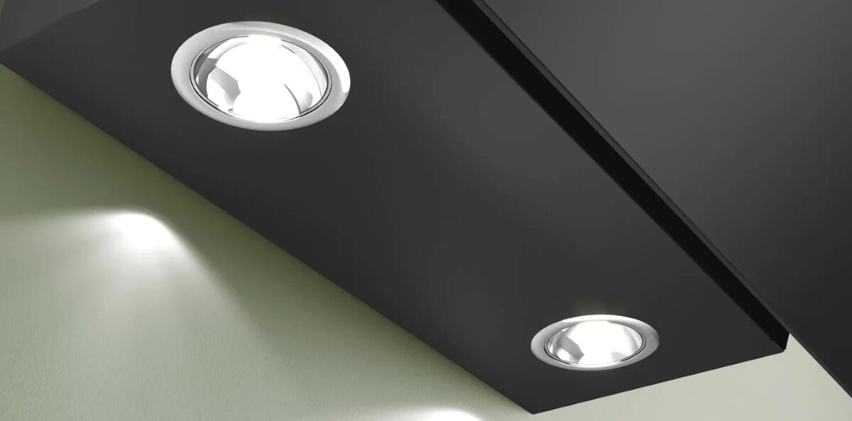 Dwa wpuszczane reflektory na czarnym suficie, oświetlające zieloną ścianę.