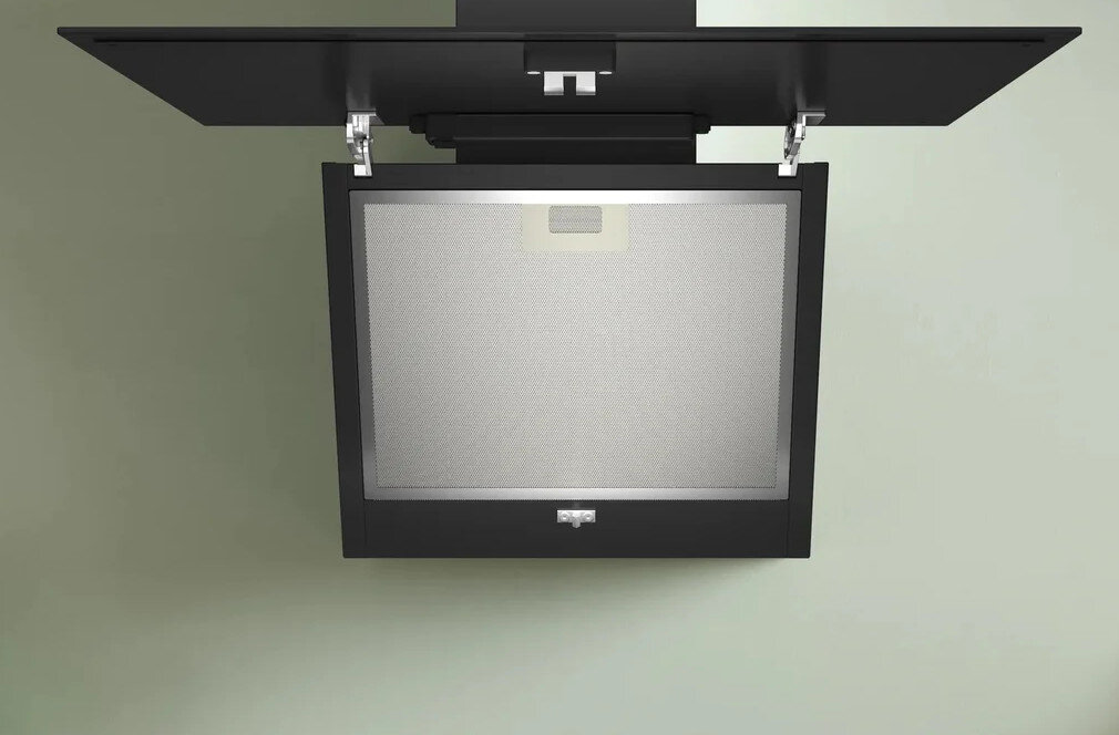 Czarny okap, obniżony panel. Srebrna krata siatkowa. Zamontowany na jasnozielonej ścianie.