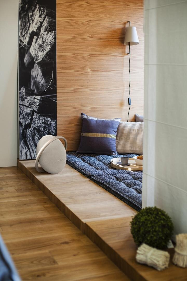 Nowoczesne wnętrze z drewnianą ścianą i podłogą. System dźwiękowy po lewej, poduszki i taca na ławce.