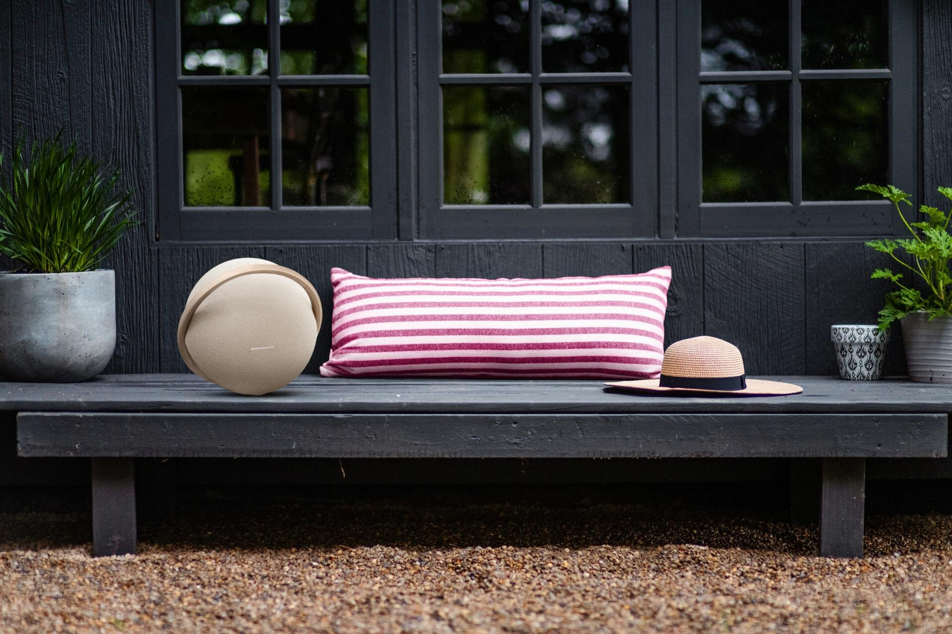Scena na zewnątrz z głośnikiem, poduszką, kapeluszem i domem w tle.