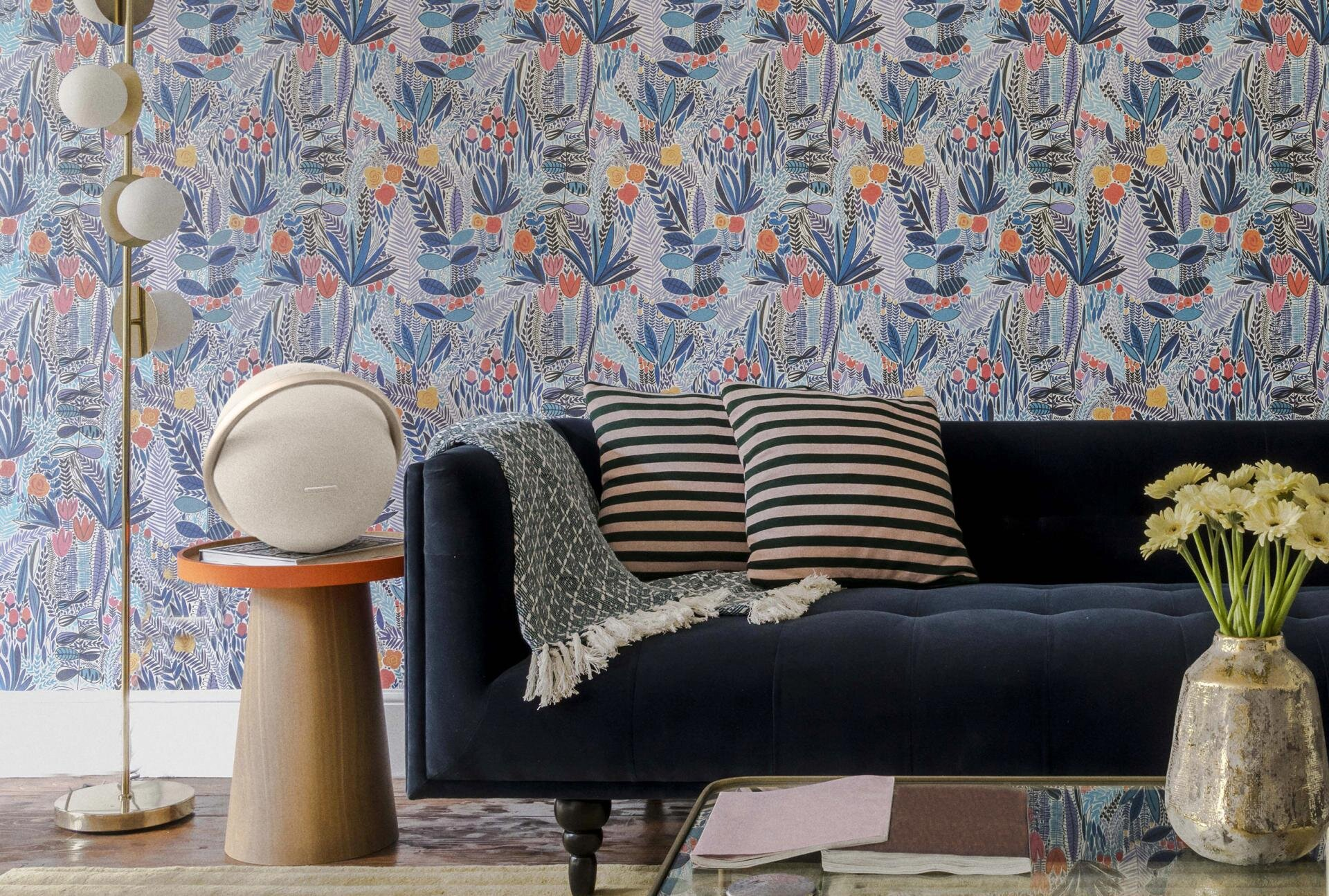 Salon z sofą, wzorzystą tapetą, głośnikiem na stoliku i poduszkami.