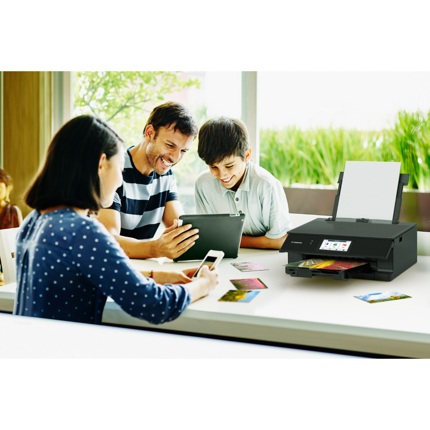 A family is gathered around a table. A printer sits on the table with photos nearby.