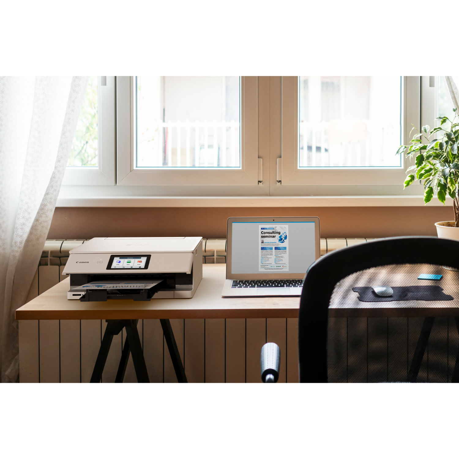 A desk with a printer, laptop, and a plant. A window and a black chair are in the background.