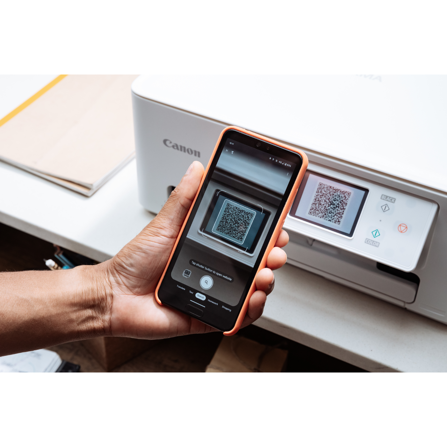 A hand holding a smartphone scanning a QR code on a printer.