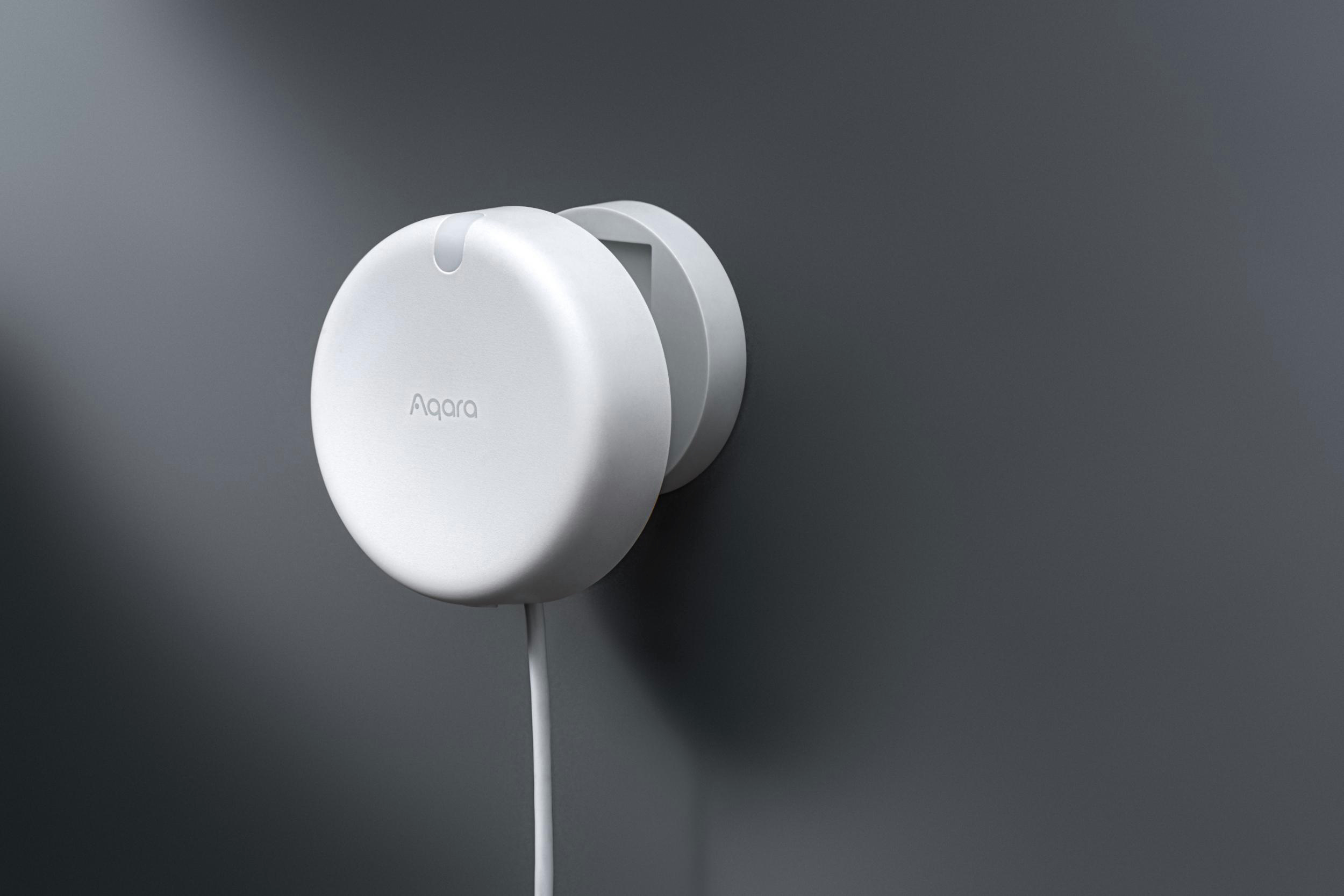 Ein weißes Aqara-Gerät an einer grauen Wand montiert.