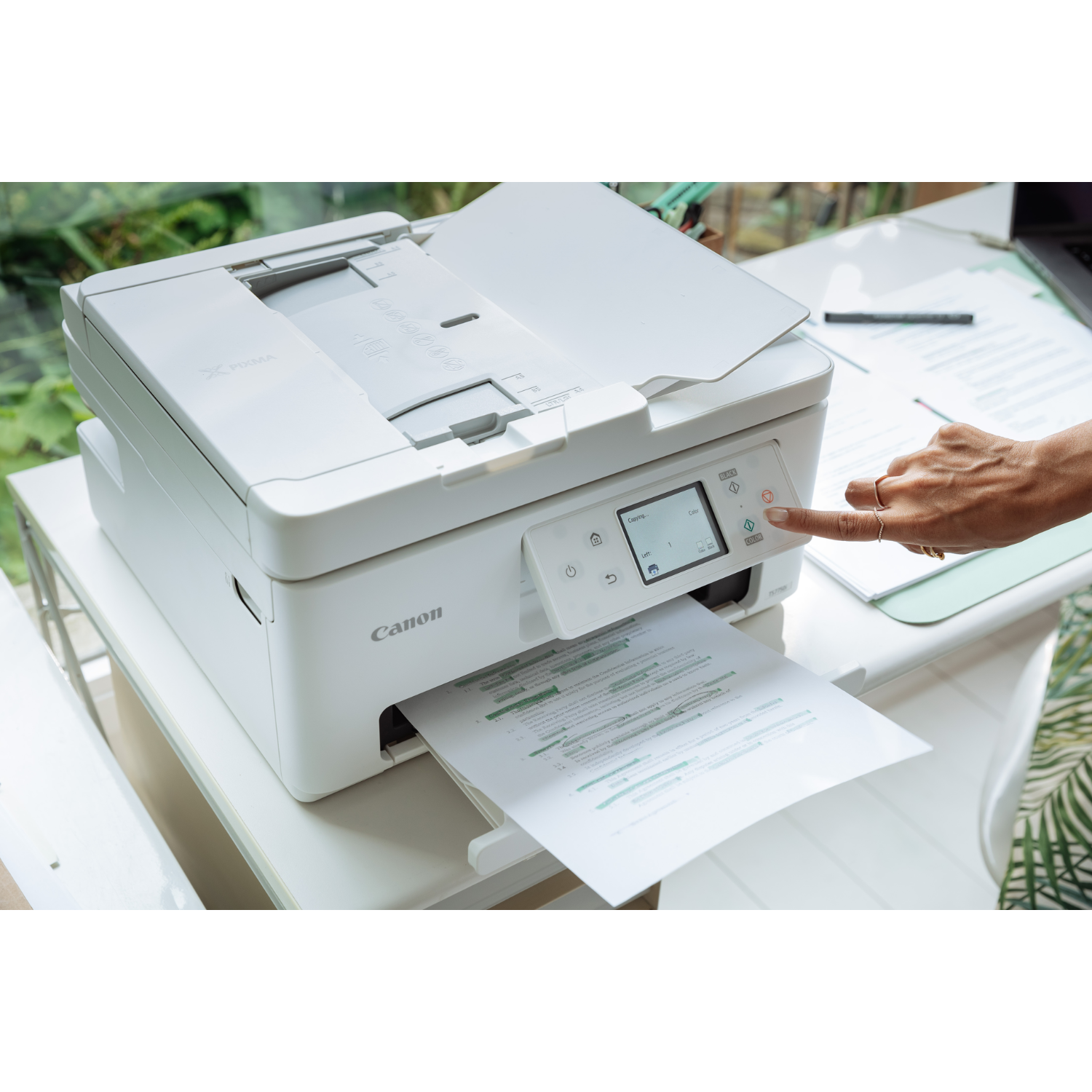 A white Canon printer with a person's hand.