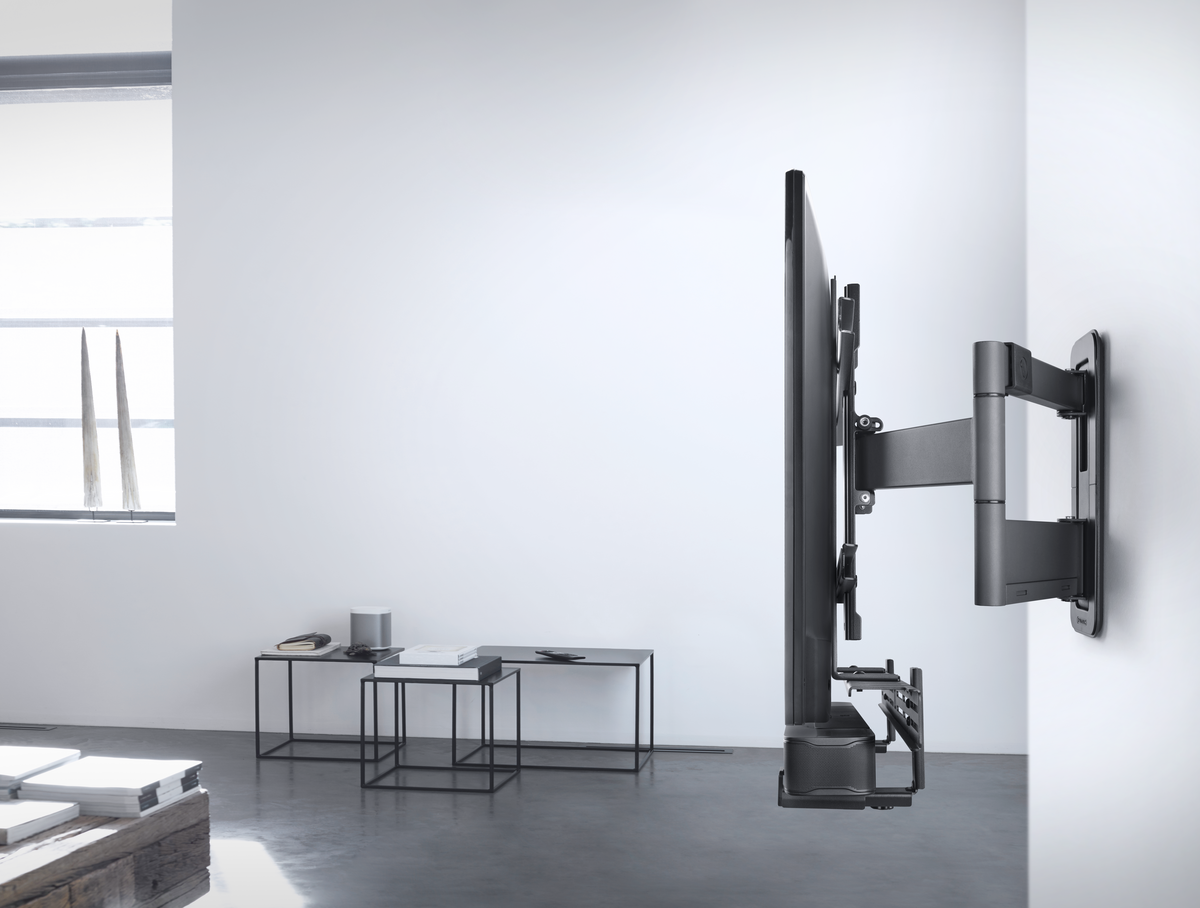 Ein großer Fernseher, der mit einer TV-Halterung an einer Wand befestigt ist. Die Wand ist weiß und der Raum hat eine einfache Einrichtung.
