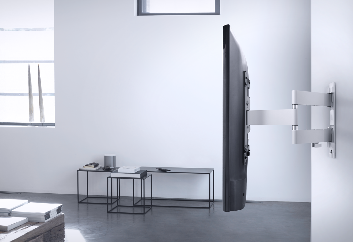 Ein modernes Wohnzimmer mit einem an der Wand befestigten Fernseher. Eine weiße Wand und ein schwarzer Tisch sind sichtbar.