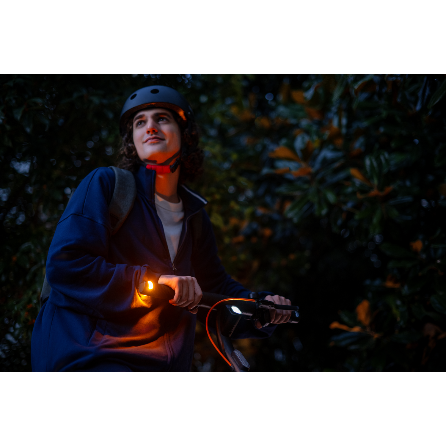 Man riding a scooter at night. He's wearing a helmet and has a light on the scooter.