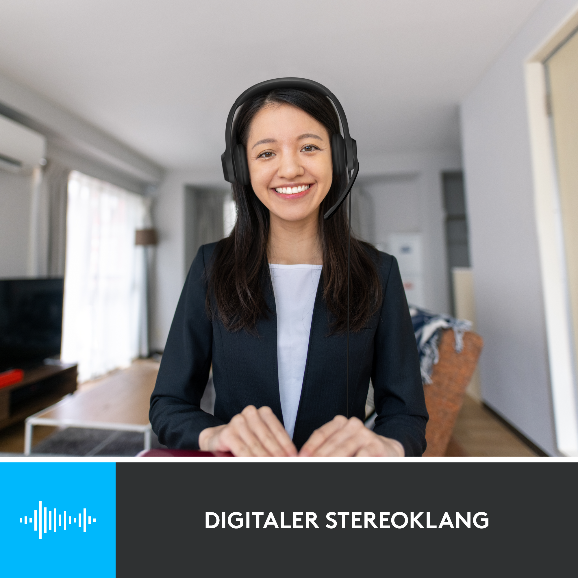 Lächelnde Frau mit Headset, schwarzem Blazer, weißem Hemd. Hintergrund zeigt Wohnzimmer.