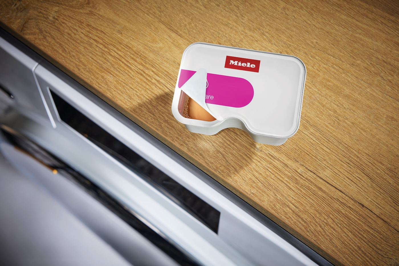 Miele Kapsel auf Holztisch, daneben eine Schublade.