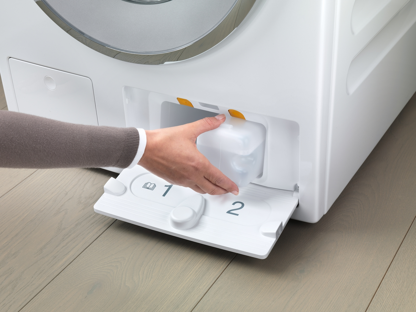 Die Hand einer Frau entnimmt einen durchsichtigen Behälter aus der Waschmittel Schublade der Maschine.