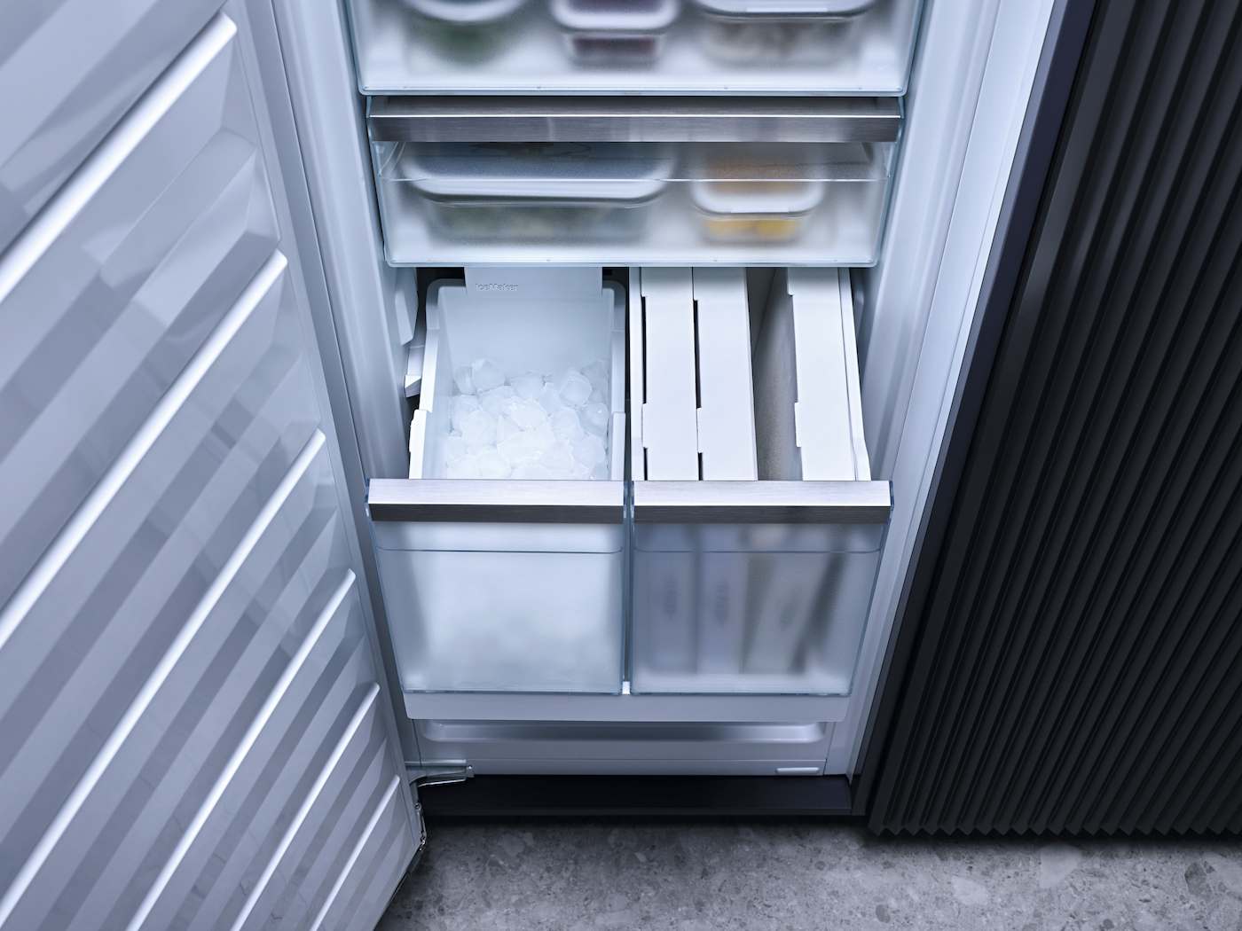 Gefrierfach mit Eiswürfeln und Behältern. Offene Kühlschranktür mit geriffelter Innenfläche.