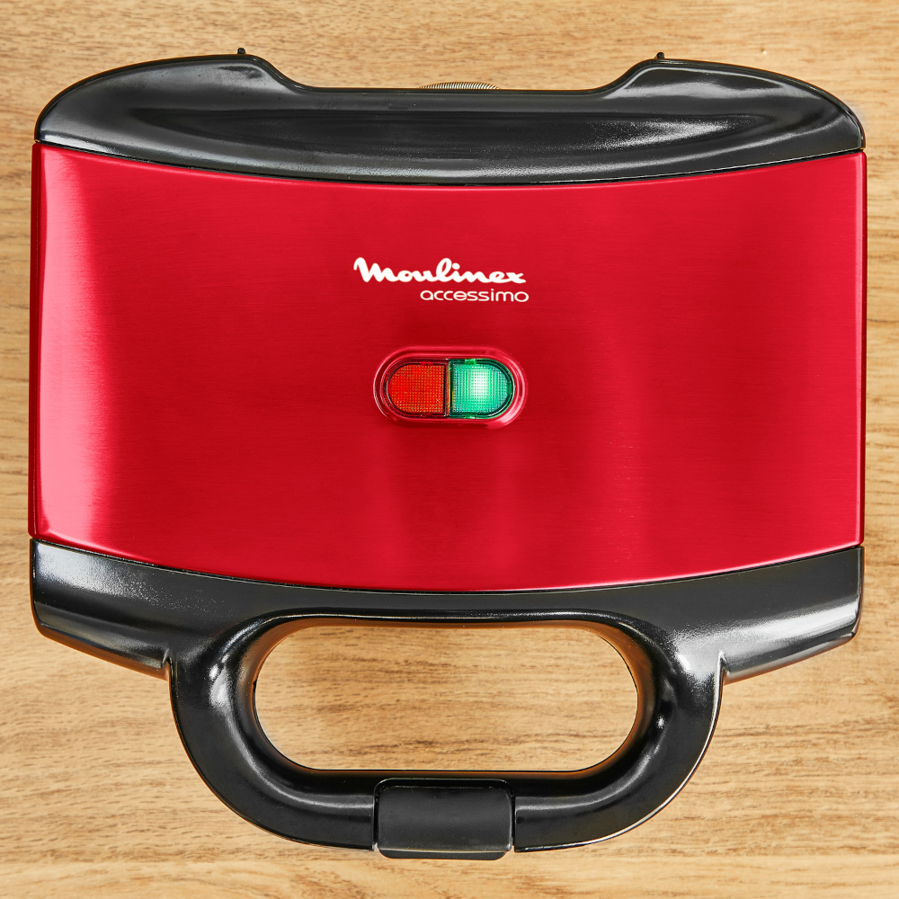 Rode Moulinex Accessimo sandwichmaker met een zwarte handgreep, op een houten oppervlak.