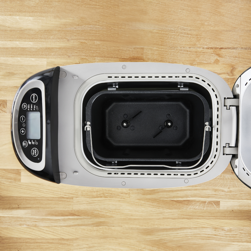 Bread maker, top view. Open, showing interior, with pan and paddles. Controls on the left.