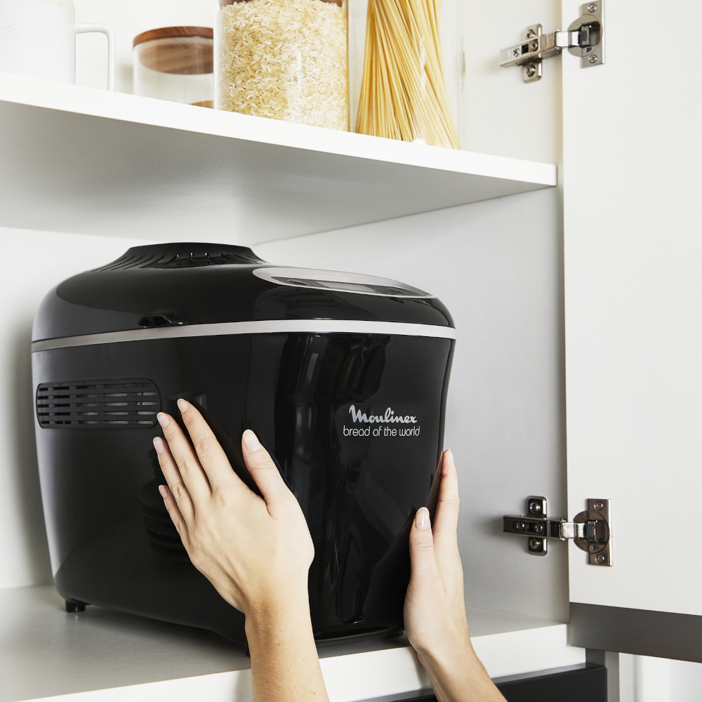 A black bread maker is being placed into a white cabinet.