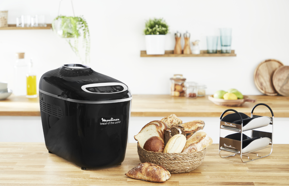 A black bread maker with bread and a basket, on a wooden counter.