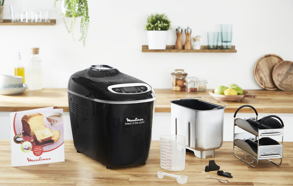 Black bread maker with accessories, white counter. Moulinex logo.
