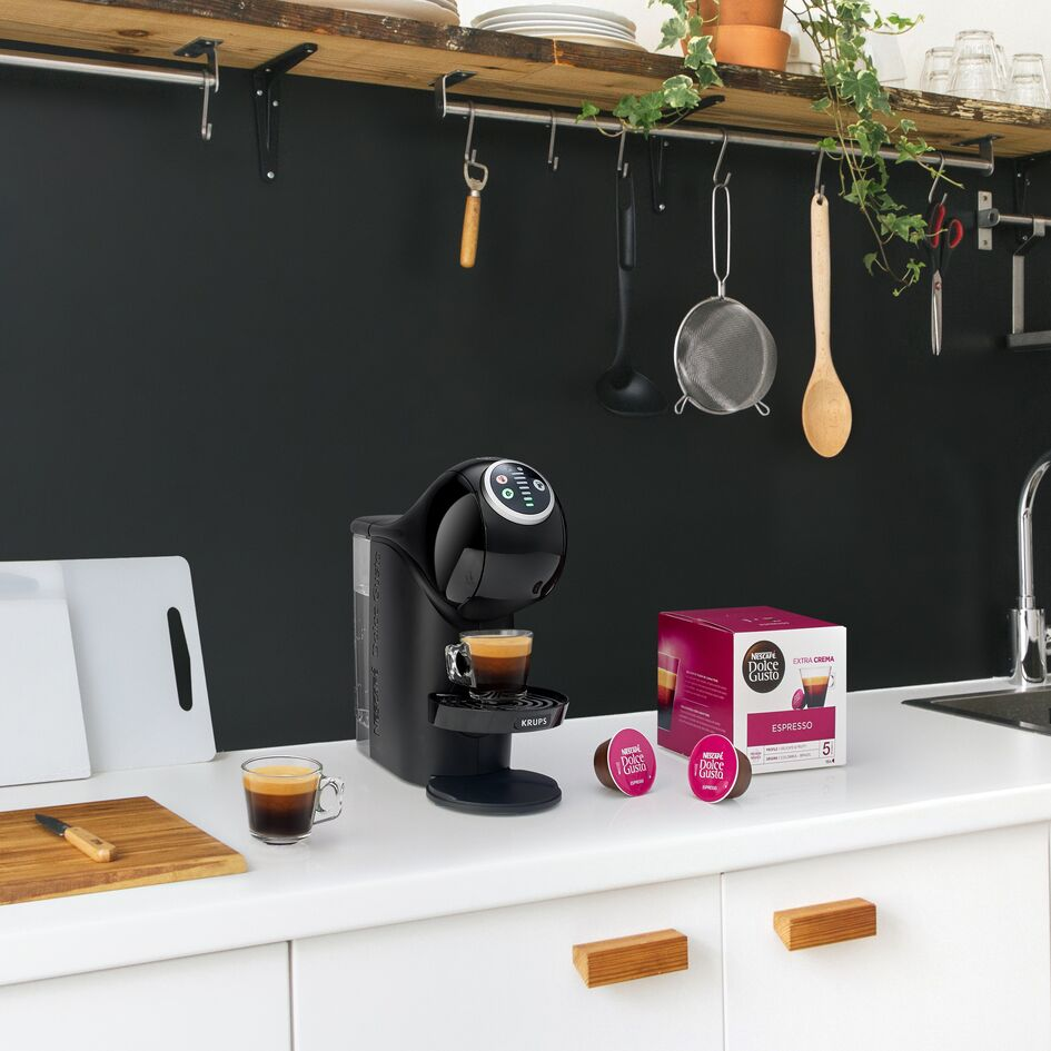 A black coffee machine with an espresso cup, and a box of coffee pods on a white countertop.