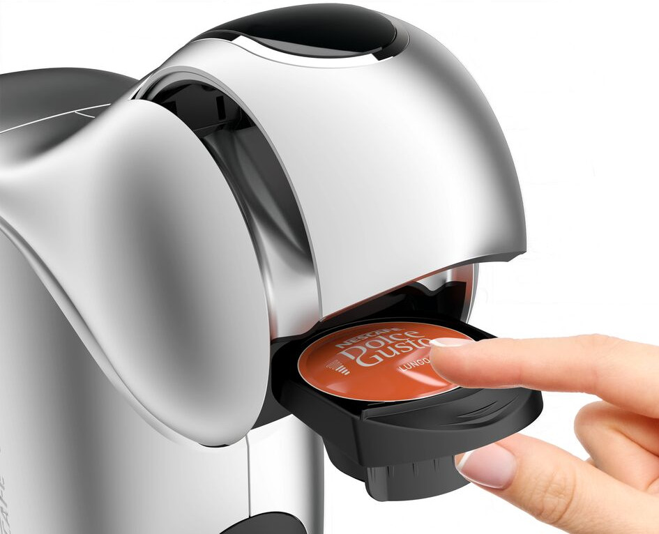Een zilveren koffiemachine met een hand die een koffiepad inbrengt.