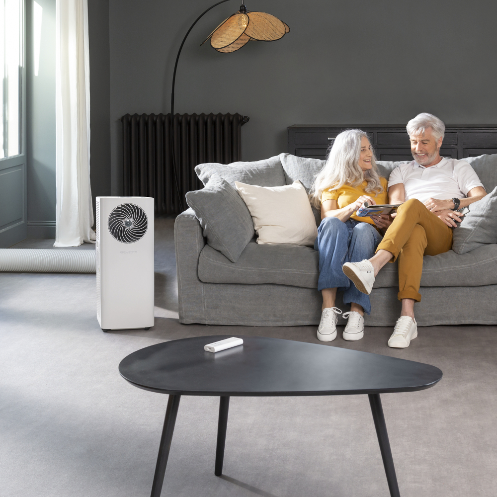 Koppel op een bank in een woonkamer. Airconditioner links, tafel ervoor.