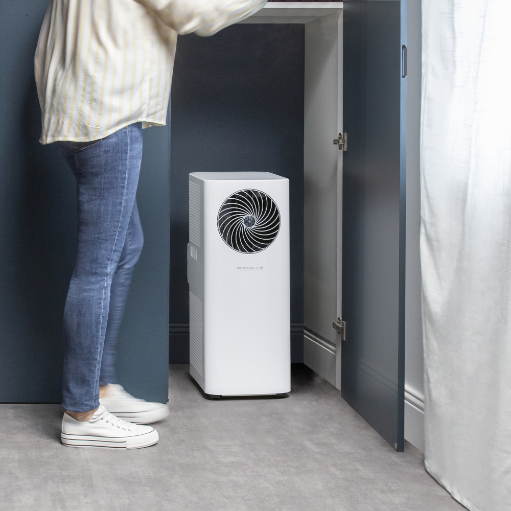 Persoon bij een witte luchtreiniger in een kamer. De deur staat open.
