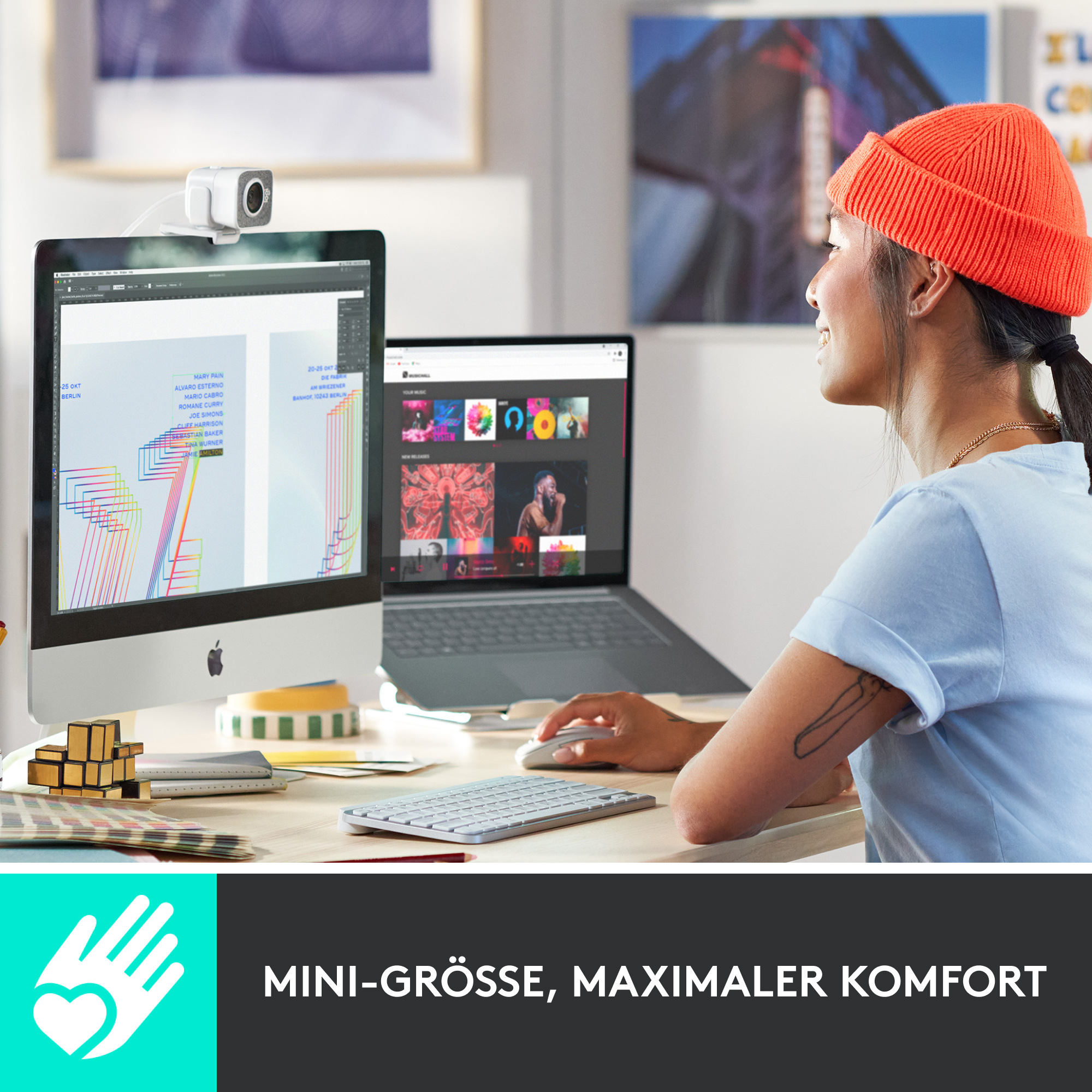 Frau mit orangefarbener Mütze nutzt Computer mit Webcam, Schreibtisch mit Monitor und Laptop.