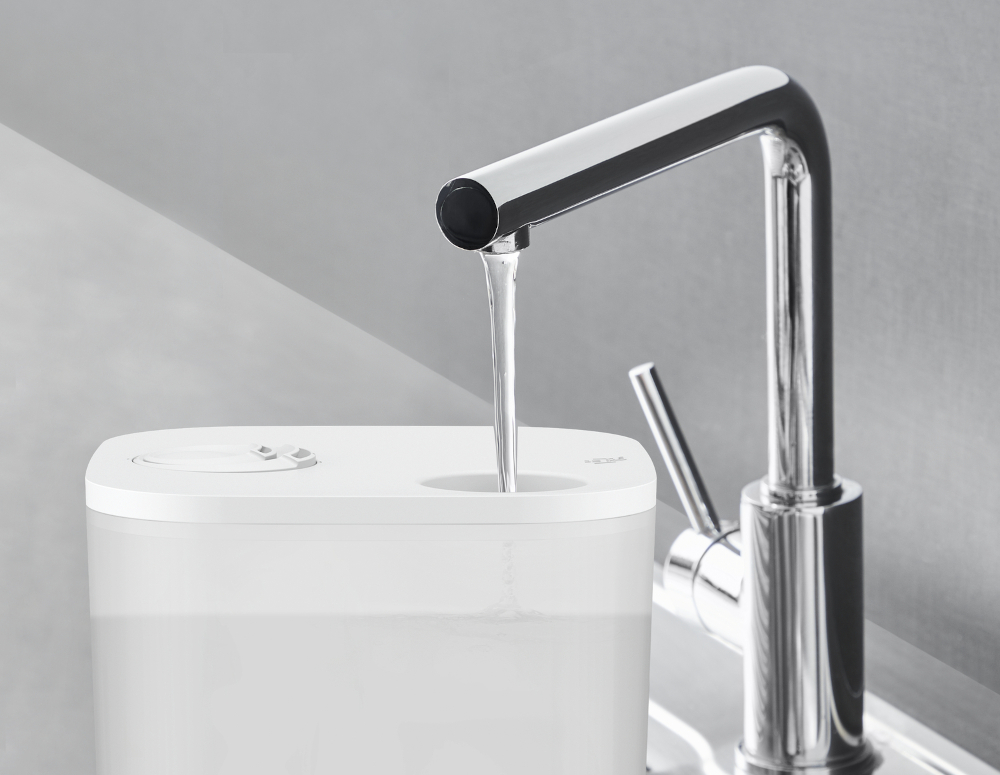 A silver faucet pouring water into a white container. The faucet is above a white rectangular base.
