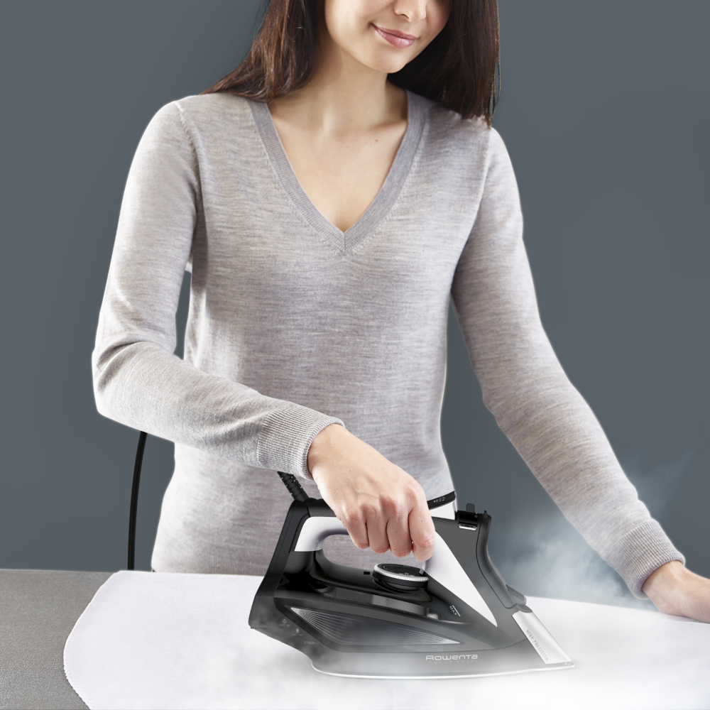Femme repassant du tissu blanc avec un fer à repasser noir. De la fumée est visible.
