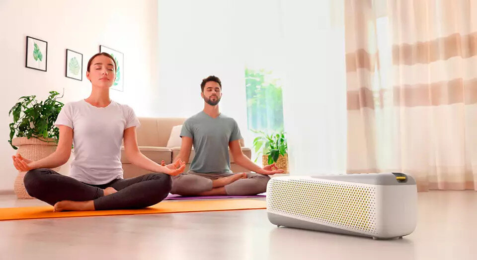 Dwie osoby medytują w pokoju, biały oczyszczacz powietrza na pierwszym planie.