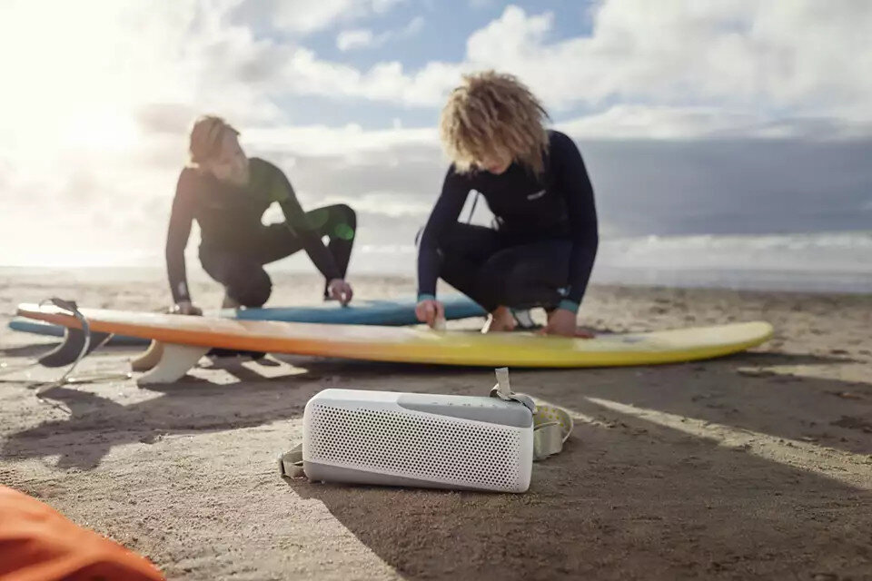 Dwóch surferów przygotowujących się na plaży z głośnikiem z przodu. Niebo jest niebieskie.
