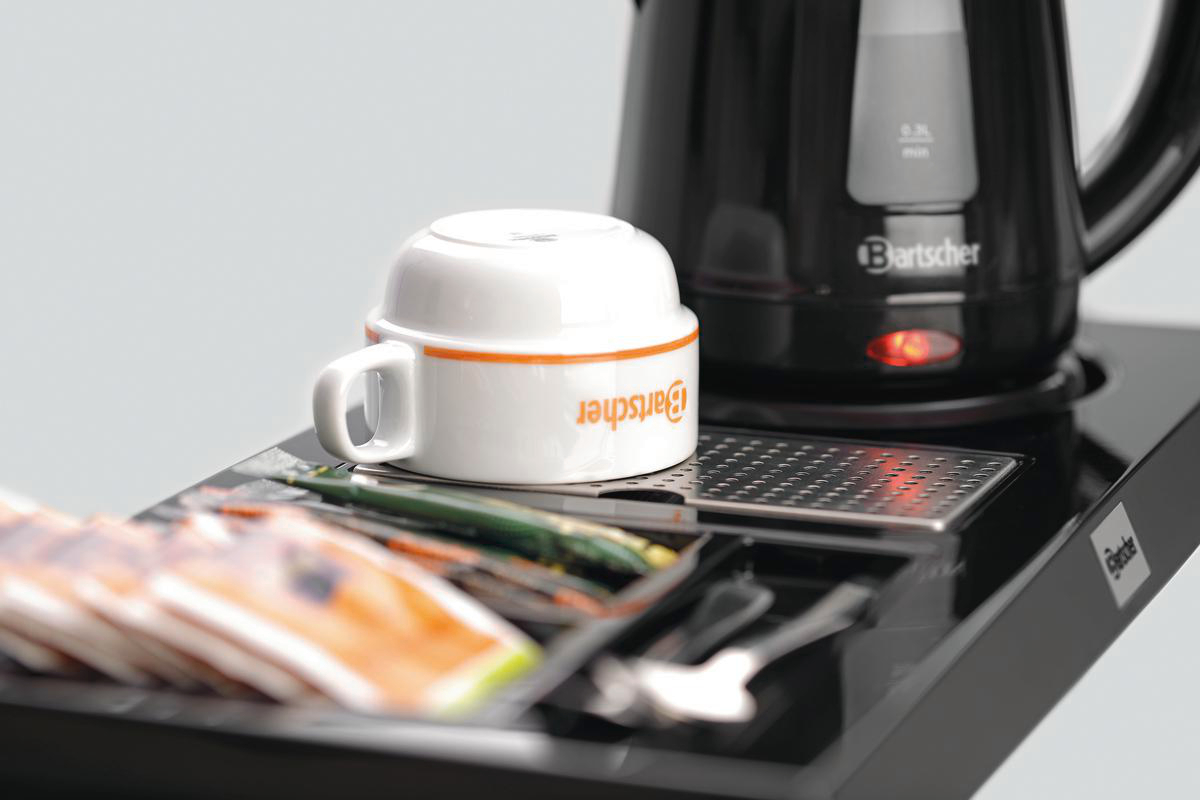 Nahaufnahme eines schwarzen Serviertabletts mit einer weißen Tasse, Teebeuteln und einem schwarzen Wasserkocher.