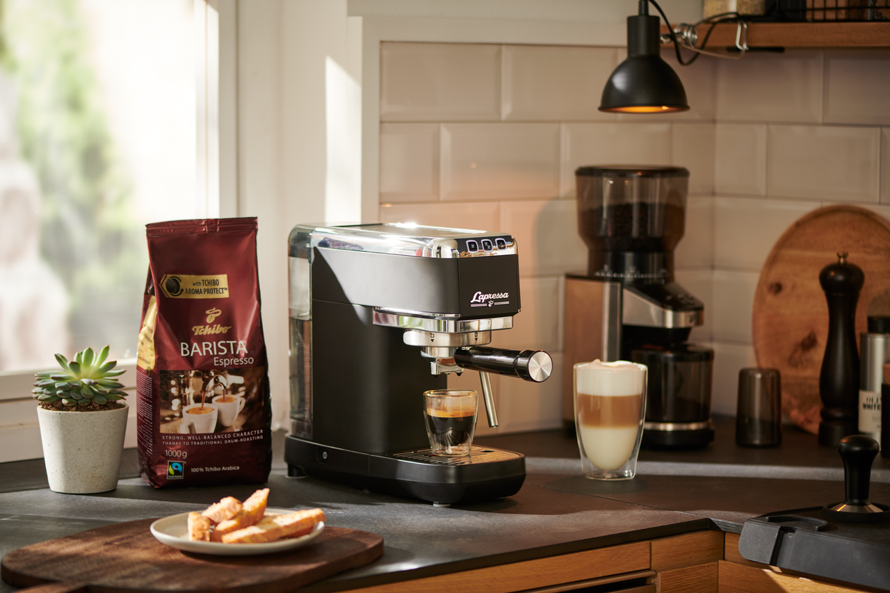 Espresso makinesi, kahve çekirdekleri, kahve fincanı ve kahvaltı yiyecekleri.