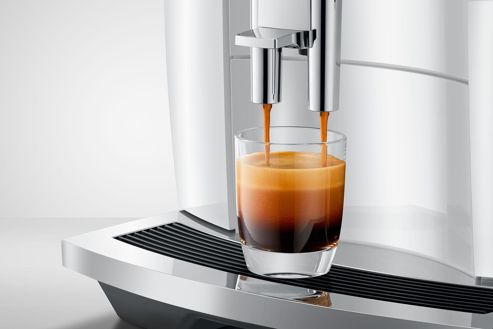 Kaffeemaschine, die Kaffee ausgibt. Klares Glas, dunkler Kaffee und weiße Maschine. Espresso wird gegossen.
