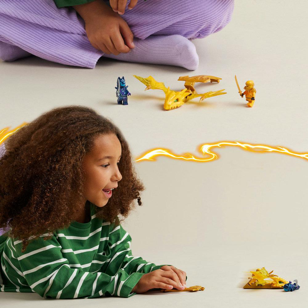 Kind betrachtet Lego Ninjago Figuren. Gelber Drache und Figuren auf weißer Fläche.
