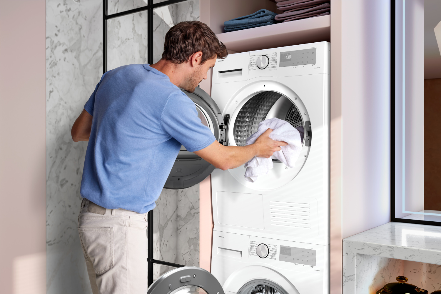 Man die een witte handdoek in een witte wasmachine laadt. Achtergrond toont een marmeren muur.